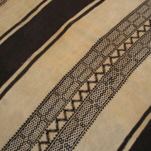 Flatweave rug detail showing alternating dark brown and tan stripes with complex geometric patterning.