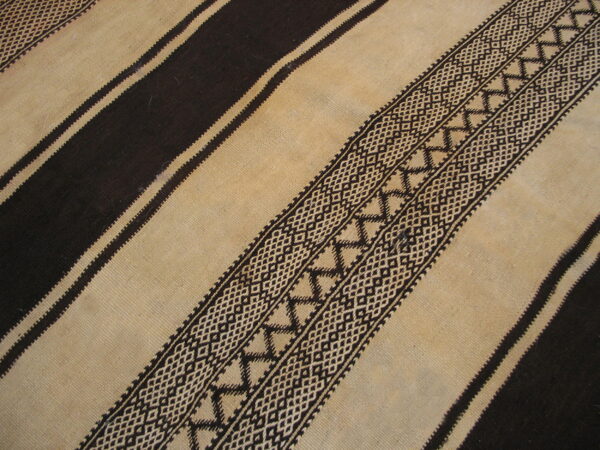 Flatweave rug detail showing alternating dark brown and tan stripes with complex geometric patterning.