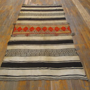 Cream and dark brown striped rug with a central orange and red geometric band on wood flooring.
