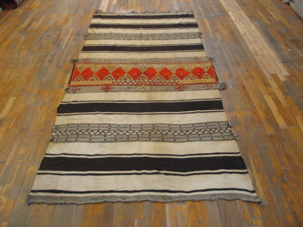 Cream and dark brown striped rug with a central orange and red geometric band on wood flooring.