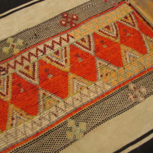 Textured runner with bright orange geometric patterns and flat-woven striped borders in tan and black on wood flooring.