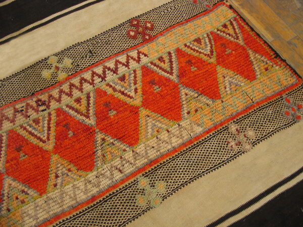 Textured runner with bright orange geometric patterns and flat-woven striped borders in tan and black on wood flooring.