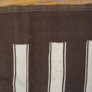 Flatweave rug in dark brown and cream with vertical stripe panels resting on wood.