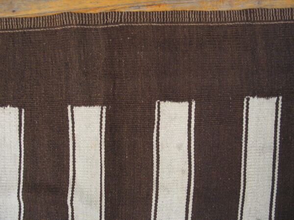 Flatweave rug in dark brown and cream with vertical stripe panels resting on wood.