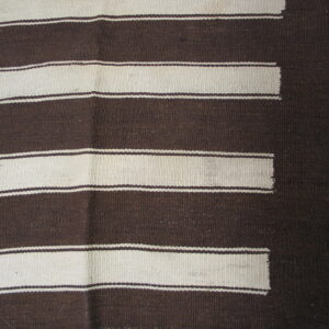 Dark brown and cream flatweave rug with wide horizontal stripes and a stepped pattern, laid on wood flooring.