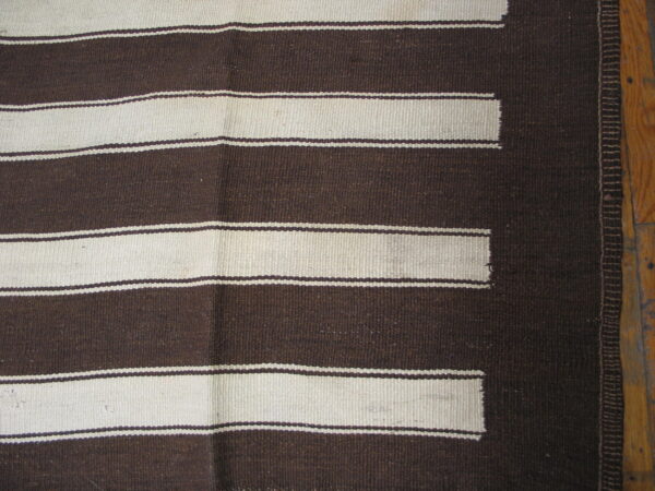 Dark brown and cream flatweave rug with wide horizontal stripes and a stepped pattern, laid on wood flooring.