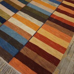 Multicolor striped flatweave rug stitched together in three panels, lying on gray-washed wooden planks.