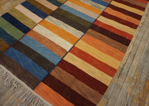 Multicolor striped flatweave rug stitched together in three panels, lying on gray-washed wooden planks.