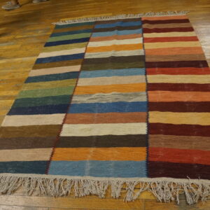 Multicolor flatwoven rug featuring three vertical sections of horizontal stripes on wood flooring.