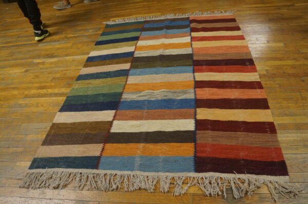Multicolor flatwoven rug featuring three vertical sections of horizontal stripes on wood flooring.