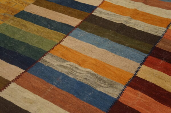 Flat woven rug with wide multi-colored horizontal stripes sewn diagonally, lying on a wood floor.