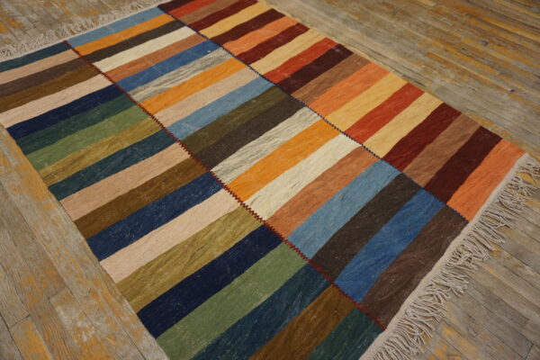 A multicolored patchwork rug featuring striped rectangular blocks rests on distressed light wood flooring.