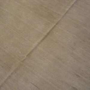 Textured tan flatweave rug with horizontal striations and a strong diagonal fold across the center.