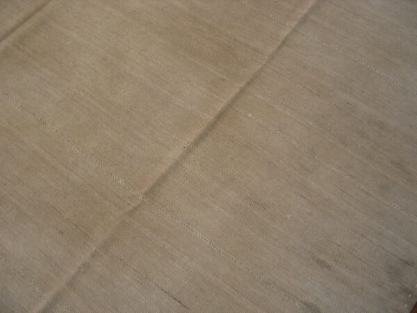 Textured tan flatweave rug with horizontal striations and a strong diagonal fold across the center.