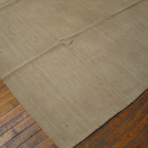 Close-up of a solid tan flatweave rug with seams placed on dark, distressed wood floorboards.