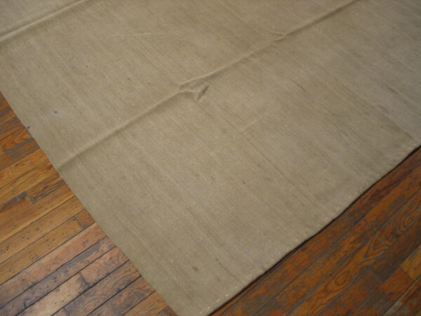 Close-up of a solid tan flatweave rug with seams placed on dark, distressed wood floorboards.