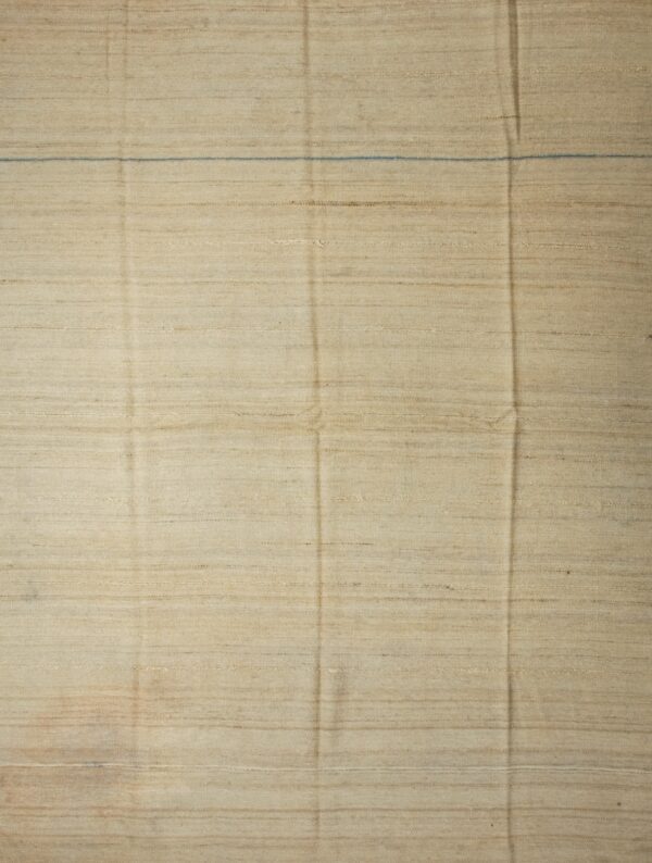 Solid cream flatweave rug with short fringes lies on worn natural hardwood flooring.