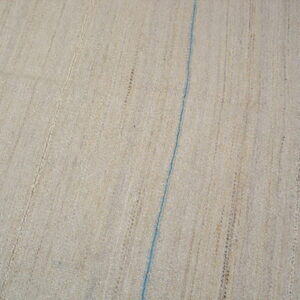 Natural flatwoven beige rug displays vertical textures and one thin blue stripe over wood floor.