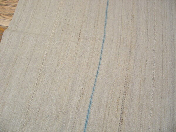 Natural flatwoven beige rug displays vertical textures and one thin blue stripe over wood floor.