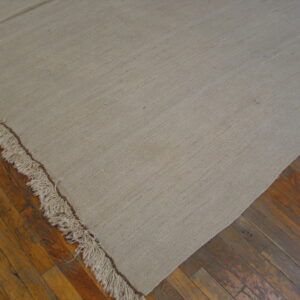 Textured beige flat-weave rug with long fringe details covers a distressed wood plank floor.