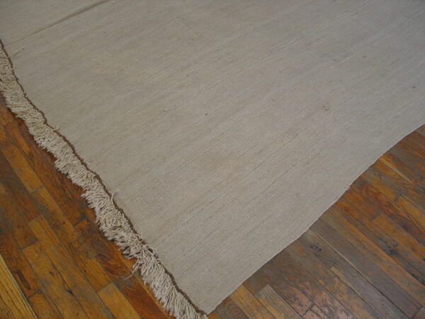 Textured beige flat-weave rug with long fringe details covers a distressed wood plank floor.