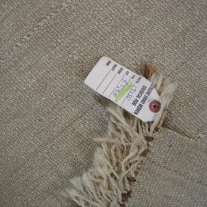 Low-pile, nubby tan rug with long cream fringe attached to a paper product tag.