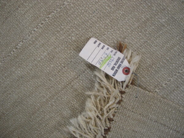 Low-pile, nubby tan rug with long cream fringe attached to a paper product tag.