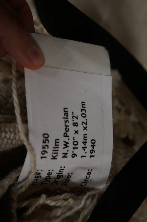 Close-up of a rug tag placed against a tightly woven beige textile showing visible cream fringe.