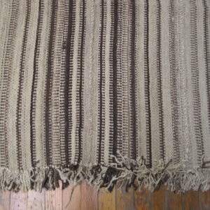 Low-pile rug featuring vertical brown and beige stripes and shaggy fringe over a wood floor.