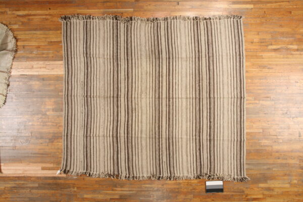 Flatwoven rug featuring light tan and dark brown vertical stripes resting on a wood floor.