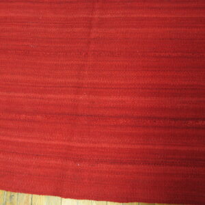 Deep red flatwoven rug displays abrash and thin dark horizontal stripes over glossy wooden floors.