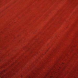 Textured, deep reddish-orange flatwoven rug with visible seams rests on a distressed wooden floor.