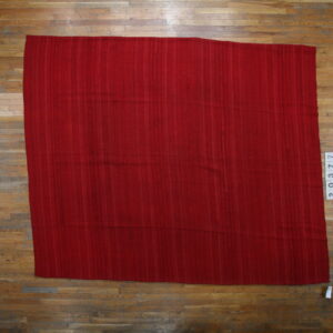 A rectangular red flatweave rug with subtle vertical striations is displayed on wide plank hardwood flooring.