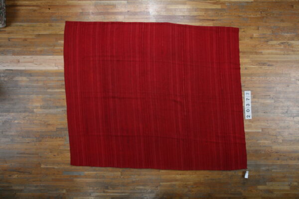 A rectangular red flatweave rug with subtle vertical striations is displayed on wide plank hardwood flooring.