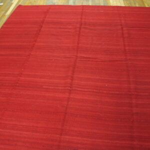 Red flatweave rug featuring subtle horizontal shading, placed on light brown wooden plank flooring.