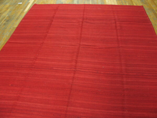 Red flatweave rug featuring subtle horizontal shading, placed on light brown wooden plank flooring.