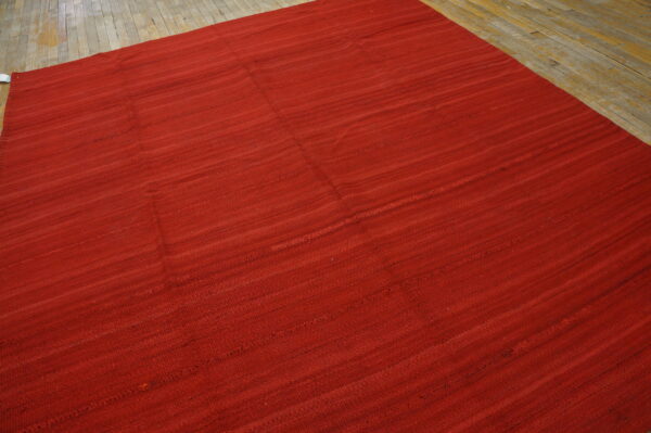 Solid red flatweave rug with visible texture placed on worn light wood plank flooring.