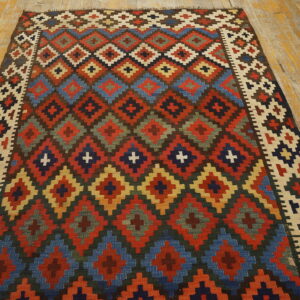 Flat-woven rug displaying multicolored stepped diamond patterns on a worn plank wood floor.