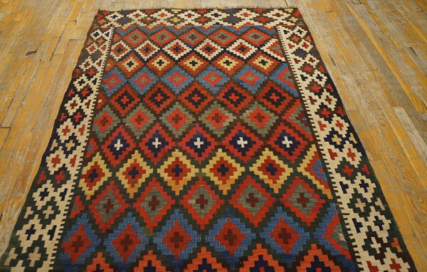 Flat-woven rug displaying multicolored stepped diamond patterns on a worn plank wood floor.