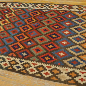 Colorful flatweave rug displaying large geometric diamonds in red, blue, orange, and tan on wood flooring.