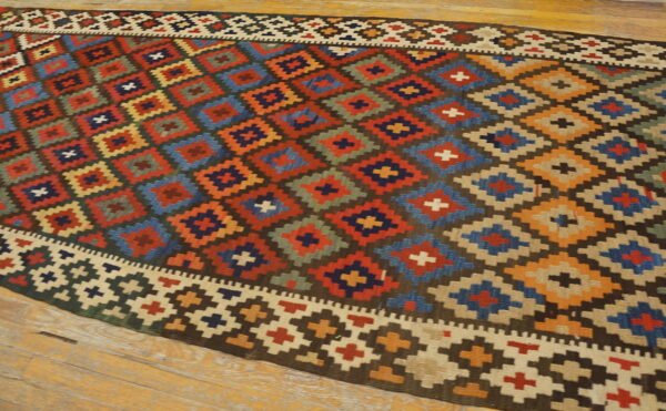 Colorful flatweave rug displaying large geometric diamonds in red, blue, orange, and tan on wood flooring.