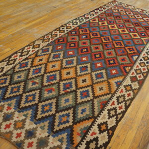 Multi-colored flatweave rug featuring stepped geometric diamond patterns on rustic, wide plank wood flooring.