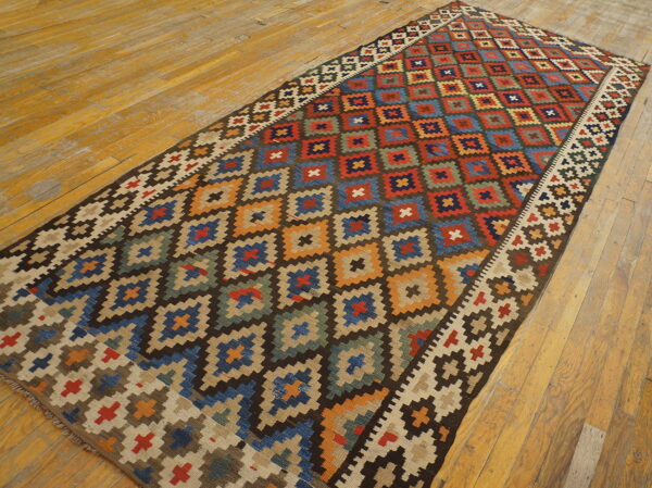 Multi-colored flatweave rug featuring stepped geometric diamond patterns on rustic, wide plank wood flooring.