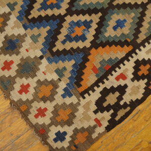 Geometric brown, blue, beige, and orange flat-weave rug corner shown on light wooden flooring.