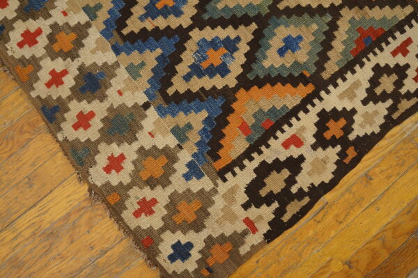 Geometric brown, blue, beige, and orange flat-weave rug corner shown on light wooden flooring.