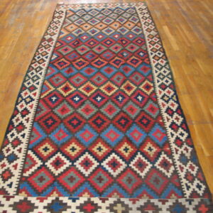Flatweave runner with vibrant red, blue, and cream geometric diamond patterns on hardwood flooring.