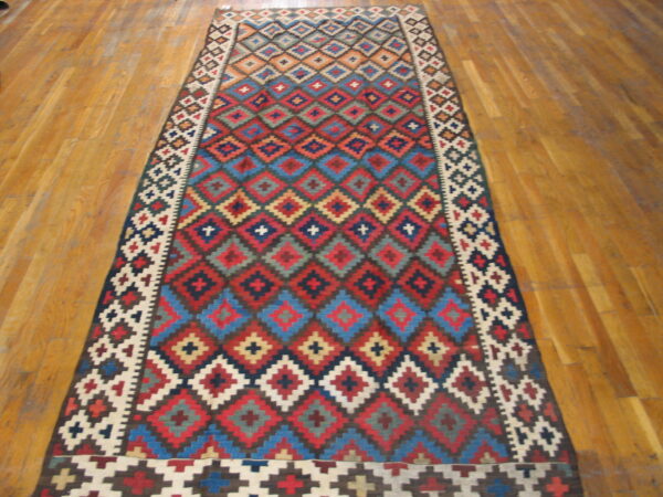 Flatweave runner with vibrant red, blue, and cream geometric diamond patterns on hardwood flooring.