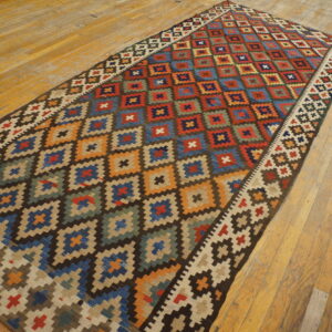 Multicolor flatweave runner rug with repeating geometric diamonds displayed on distressed wood floors.