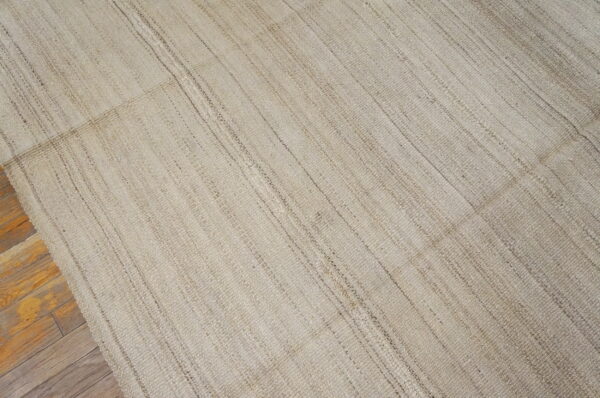 Natural beige woven rug with subtle vertical texture variations rests on hardwood floors.