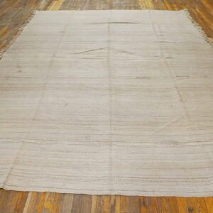 Neutral flatweave rug featuring faint horizontal light brown stripes displayed on distressed hardwood flooring.